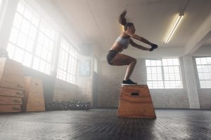Side view image of fit young woman doing a box jump exercise. Muscular woman doing a box squat at the cross fit gym